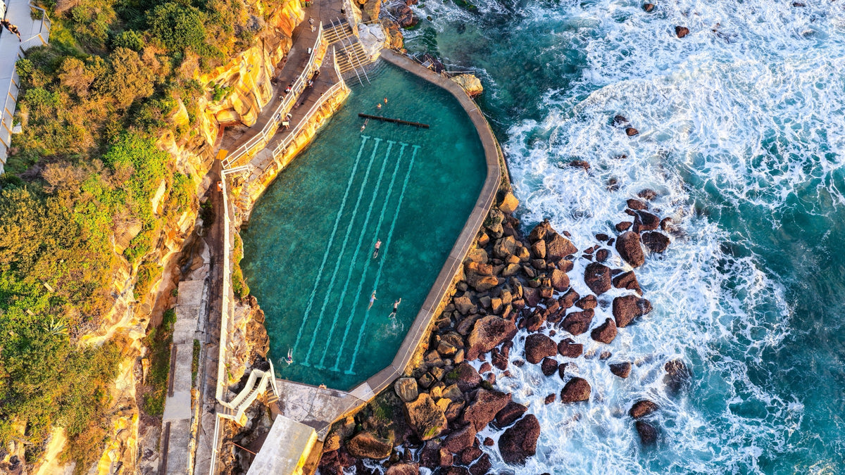 Bronte Baths ocean pool from above, cut into the cliff with waves breaking beside it, Sydney