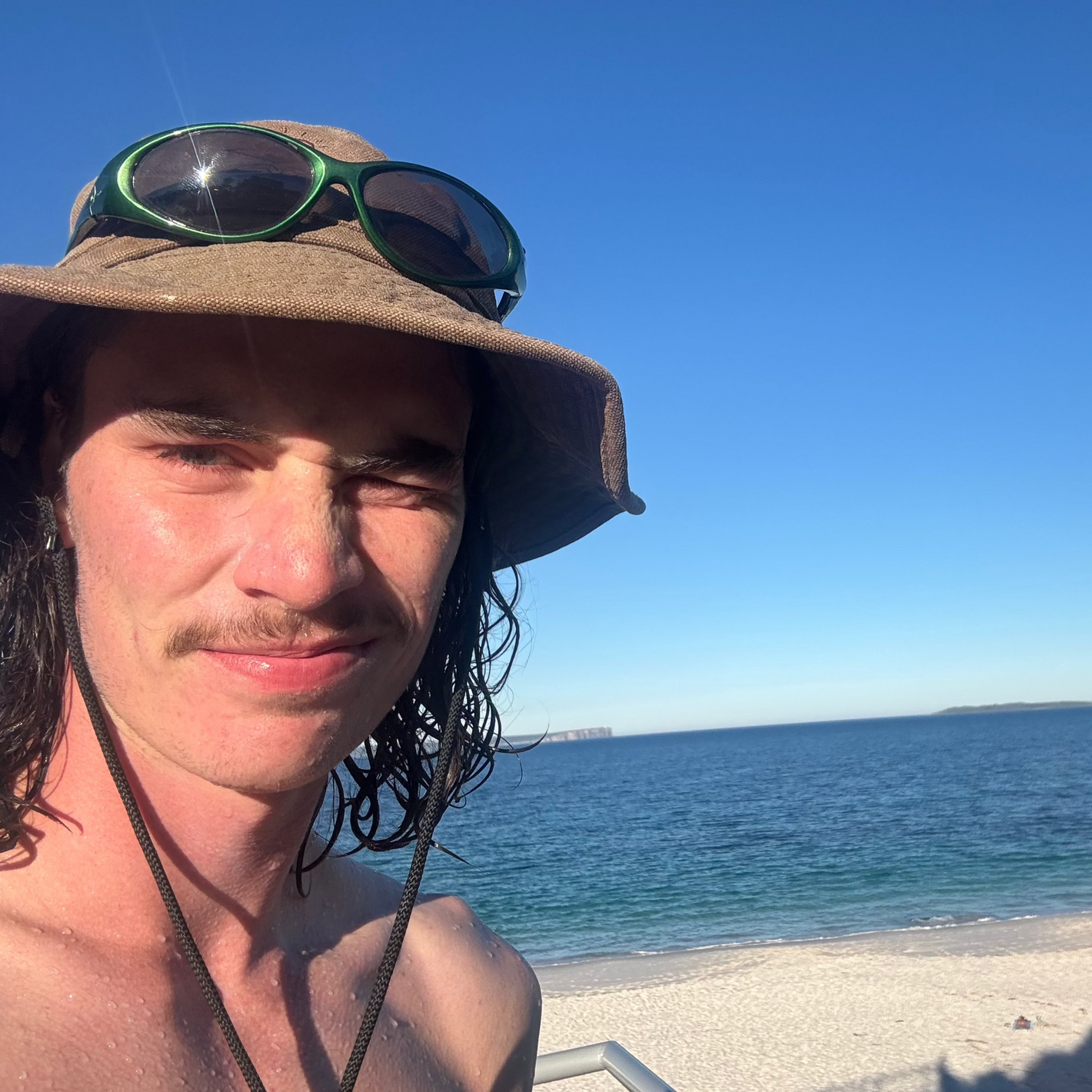 Young man taking a selfie at a remote beach with clear blue water, found using the Sole Drift map.