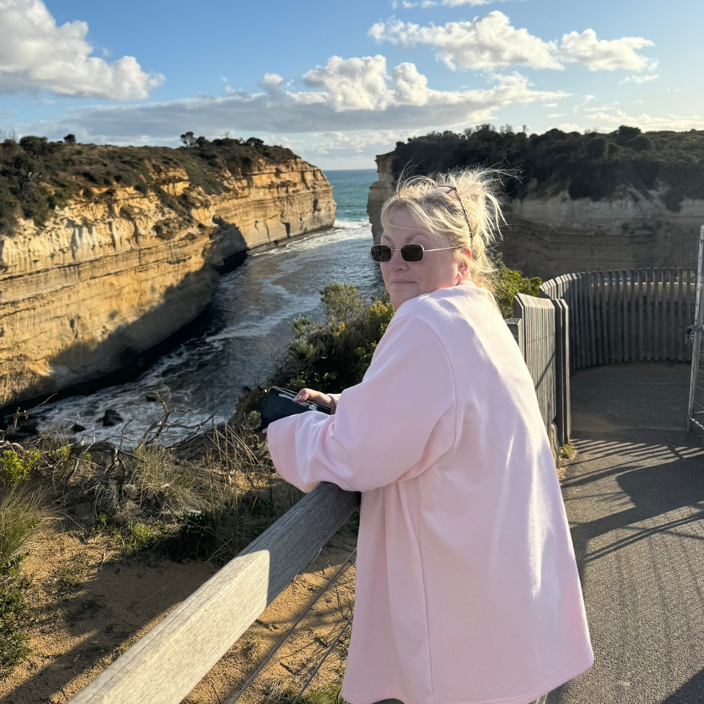 Woman using the Sole Drift map while enjoying coastal cliff views at a lookout platform on the Great Ocean Road, Australia.