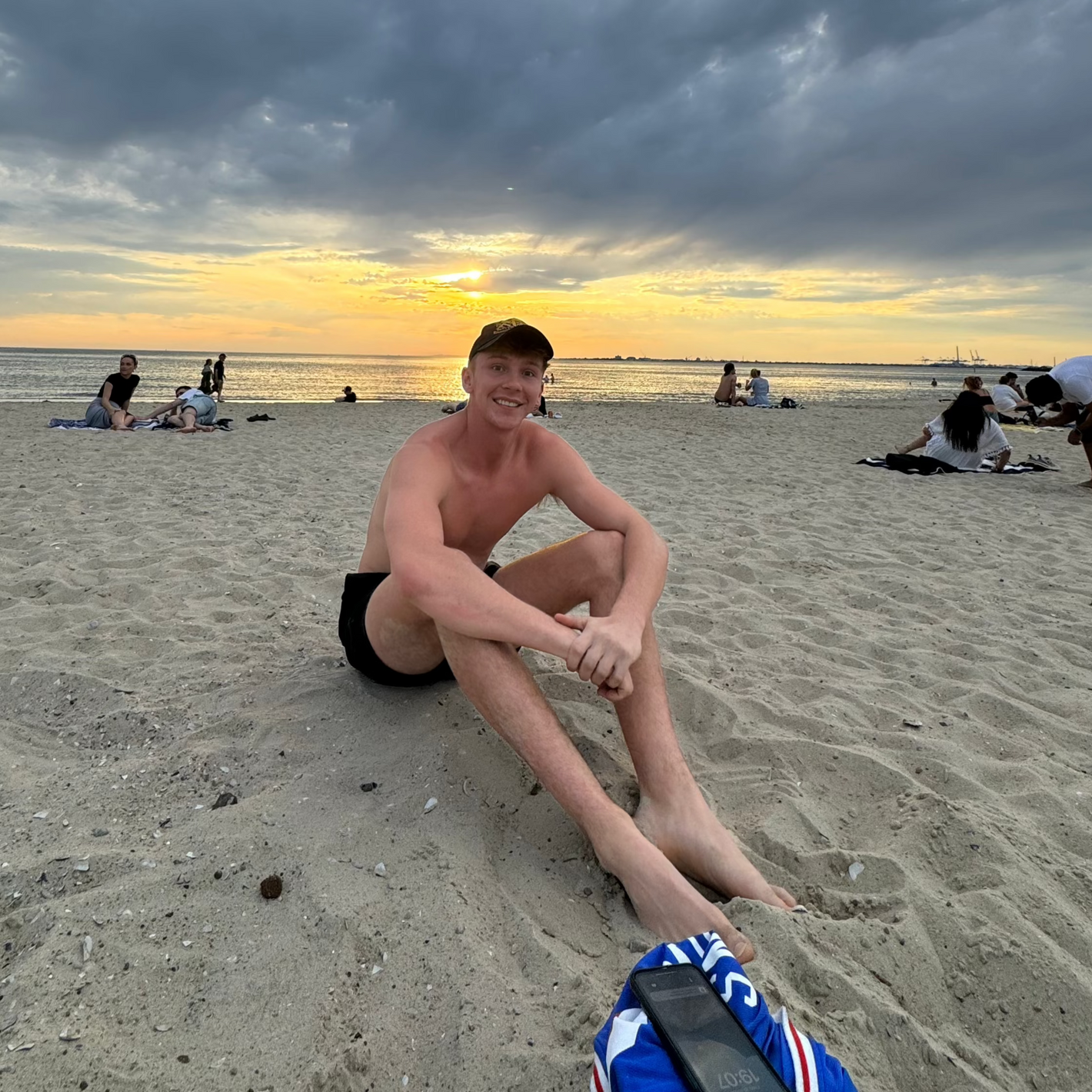 Man sitting on a sandy beach at sunset, smiling after discovering the location using the Sole Drift map.