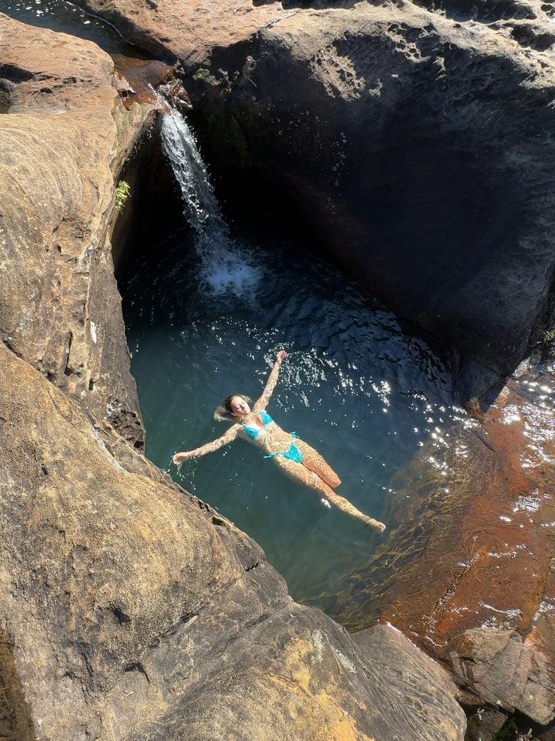 Swimmer floating in a deep rock pool below a small waterfall at Blackdown Tableland, Queensland, Australia