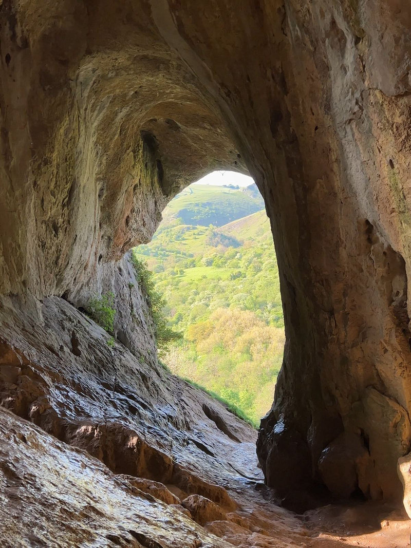 View out of the arched mouth of Thor's Cave over green hills in the Peak District, UK
